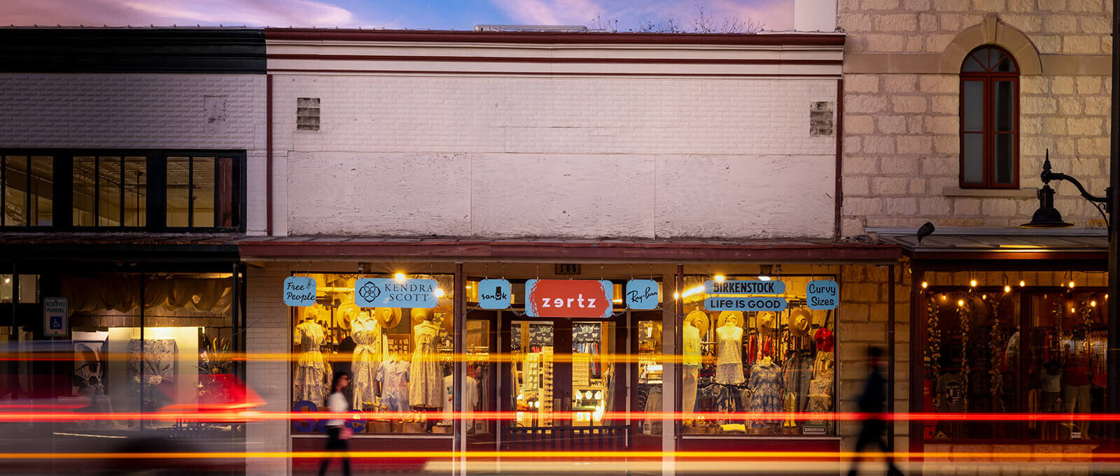 Zertz Boutique storefront on Main Street at dusk, lit windows and car light trails streaking past